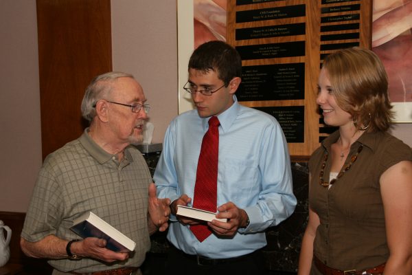 professor presenting book to two students